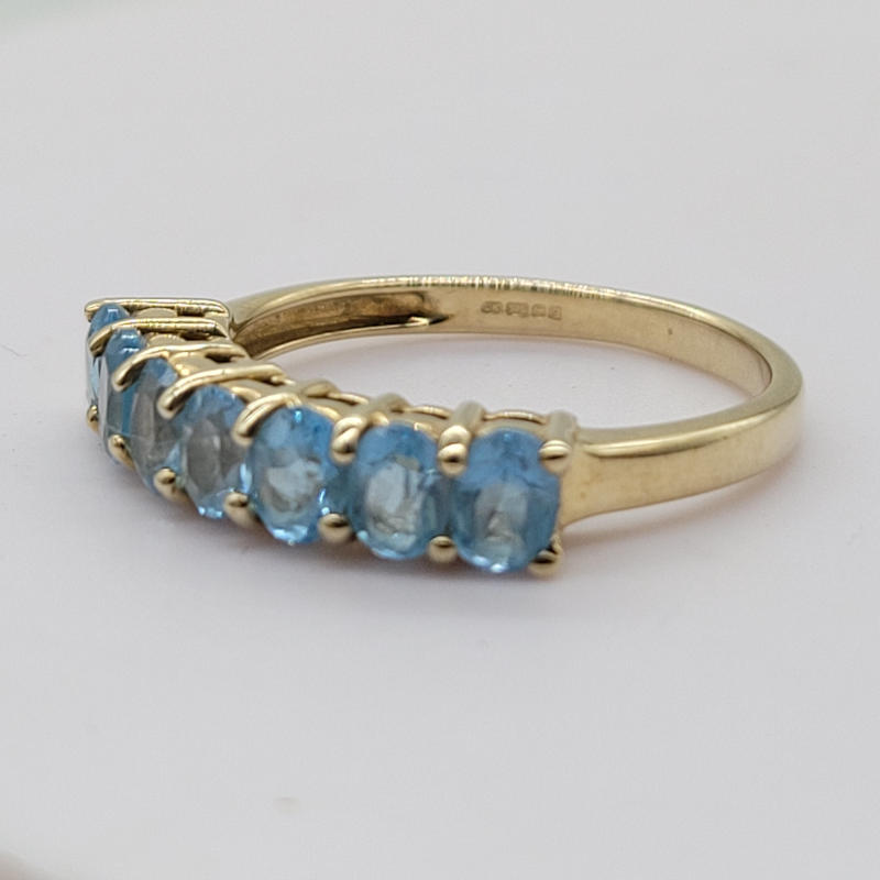 A chunky 9ct yellow gold half eternity ring with 7 raised aqua blue oval cut topaz stones. UK Size N