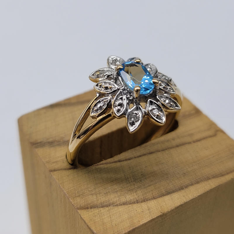 Blue Topaz & Diamond Flower Ring A bright and sparkly ring with an oval shaped blue topaz (approximately 0.75K) with small diamonds set in the petals of the flower design. All set in a 9ct yellow gold setting. The stones are all claw set in this gorgeous cocktail-style ring. UK Size P US Size 7¾ Circumference 56mm