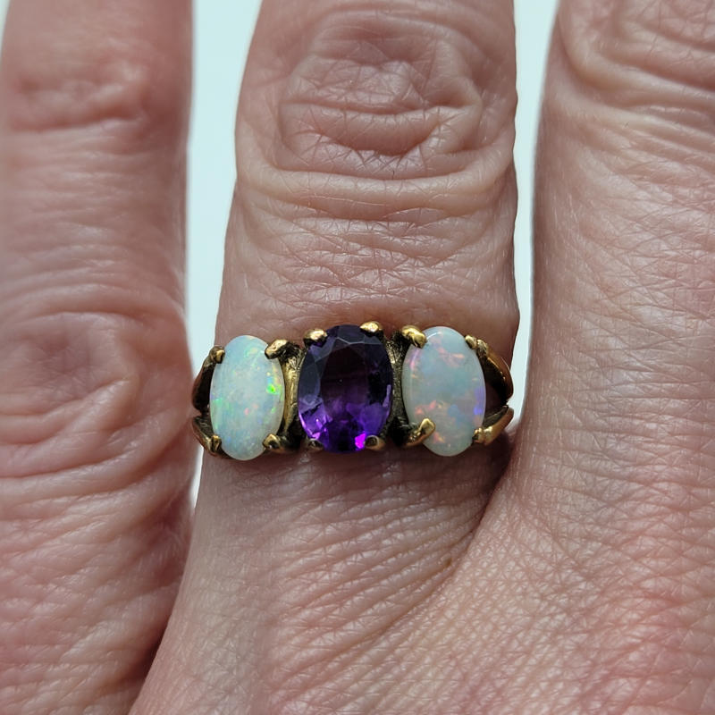 9ct Amethyst Opal Trilogy Ring A beautiful 9ct yellow gold ring with 2 white opal gemstones on either side of a central purple amethyst gemstone. The trilogy of stones are all oval in shape. UK Size N½ US Size 7 Circumference 54.5mm