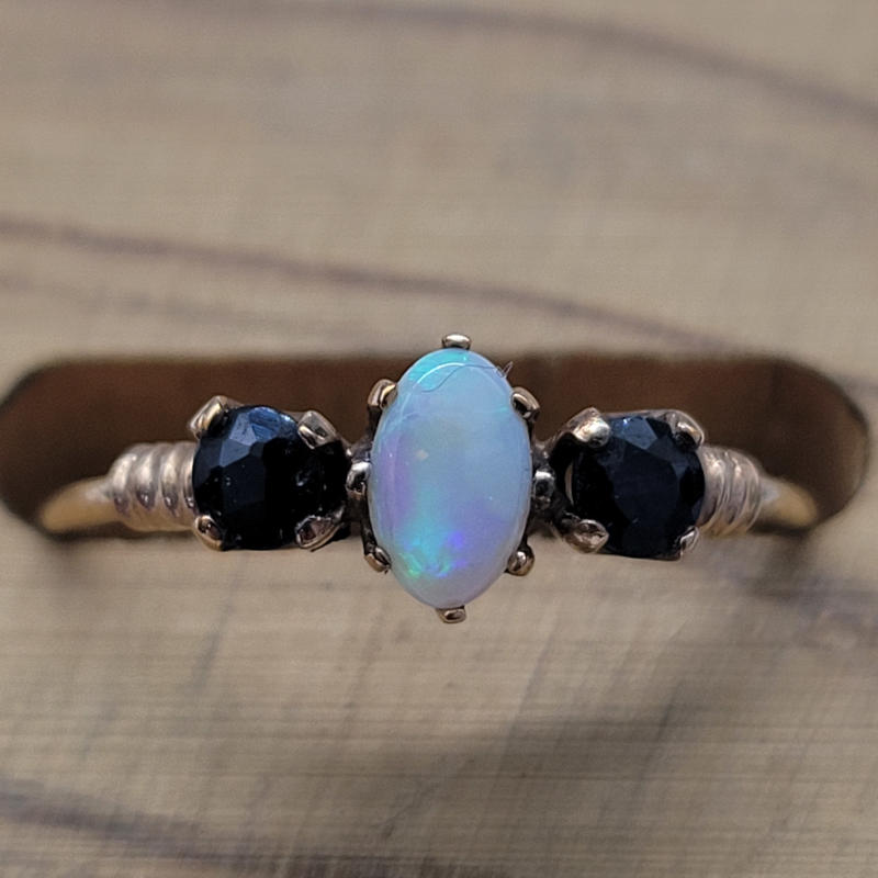 Vintage 9ct Yellow Gold Opal and Sapphire Trilogy Ring A delicate 9ct yellow gold trilogy ring with an oval opal to the centre and a round sapphire on each side. All gems are individually claw set. Hallmarked Birmingham 1956 UK Size J US Size 4¾ Circumference 49mm
