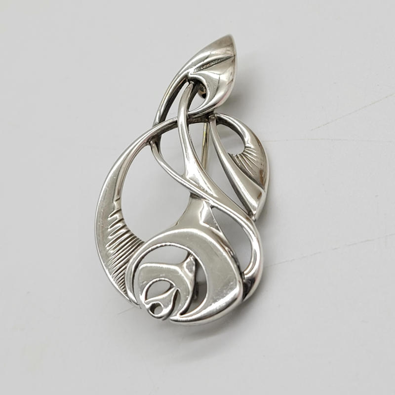 Ola Gorie Silver Rose Brooch A silver celtic brooch in an art nouveau and geometric Glasgow rose style. Made by Ola Gorie. Ola Gorie is a renowned jewellery designer and silversmith from Orkney, Scotland. She is known for her exquisite designs inspired by the rich history and natural beauty of the Orkney Islands. Ola's work often incorporates traditional Celtic and Norse motifs, as well as elements of the surrounding landscape, such as the sea, sky, and wildlife. Her attention to detail and craftsmanship have earned her numerous accolades and recognition in the world of jewellery design. Ola Gorie's creations are highly sought after by collectors and enthusiasts alike, and her pieces can be found in galleries and museums worldwide. Measures 5cm x 2.5cm