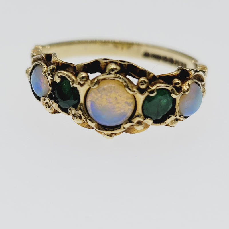 9ct Ornate Opal & Emerald Ring This exquisite 9ct yellow gold ring boasts a stunning ornate design adorned with five beautiful gemstones. The ring features an opal cabochon as the main stone, complemented by an emerald on either side and other opal gemstones on either side of the emeralds. The prong setting style further enhances the beauty of the ring, making it a perfect gift for any occasion, including Mother's Day, Christmas, graduation, anniversary, birthday, and Valentine's Day. The ring is signed and hallmarked by GT&J, a trusted brand in fine jewellery. The band width measures 3mm, and the main stone measures 5mm in diameter. This ring is a perfect addition to any jewellery collection and is sure to make a statement. An ornate 9ct yellow gold ring with 3 round opals and 2 round emeralds, the central opal is the largest whilst the other stones are all the same size. UK Size O US Size 7¼ Inner circumference 55mm